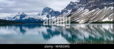 Al Lago Bow - Panoramico nuvoloso giorno di primavera vista delle cime innevate che riflette nella calma e colorata Bow Lake, il Parco Nazionale di Banff, AB, Canada. Foto Stock