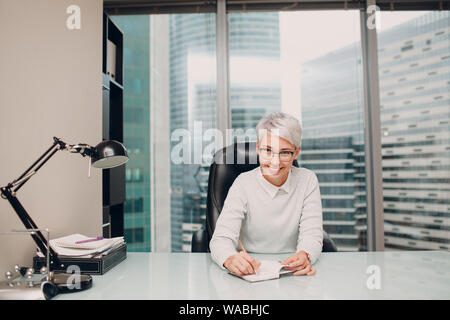 Ritratto di un giovane ed elegante specialista femmina con gli occhiali seduto al tavolo. Psicologo, avvocato, banchiere, concetto manager. Foto Stock