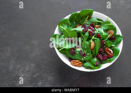 Insalata di spinaci con noci pecan e mirtilli rossi secchi su sfondo scuro, copia dello spazio. Pulire Heathy vegan cibi crudi, insalata fresca. Foto Stock