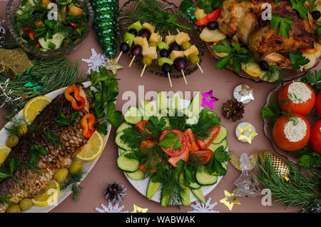 Vacanze di Natale in tavola con pollo, pesce, verdure, tartine, decorato con rami di conifere, fiocchi di neve, le decorazioni di Natale Foto Stock