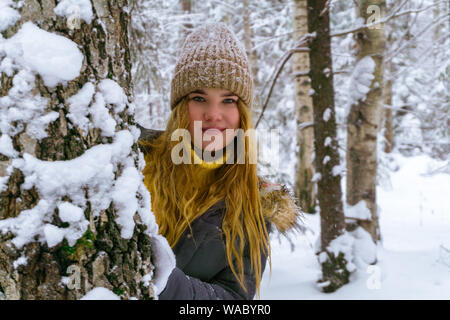 Allegro ragazza in un winter park è sorridente, spiata da dietro a un albero Foto Stock