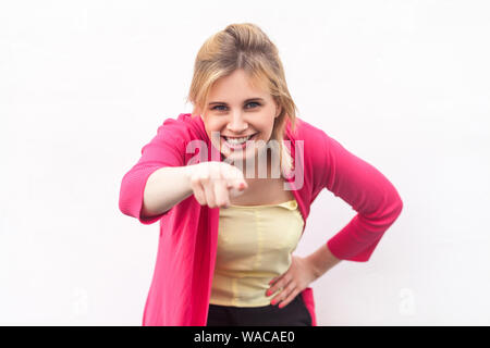 Ritratto di felice bella ragazza bionda in maglietta gialla e rossa camicetta in piedi, di puntamento e guardando la telecamera con sorriso toothy. piscina studio Foto Stock