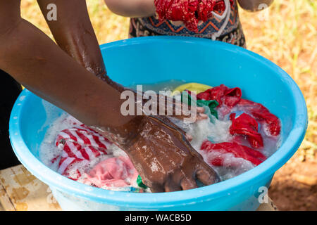 Nanyuki, Kenya - Giugno 13th, 2019: fotografia a colori della donna keniota il lavaggio a mano di biancheria in vaso blu con le mani solo visibile. Foto Stock