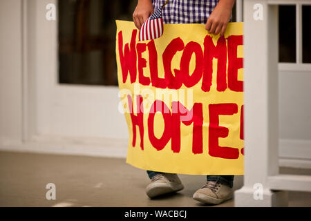 Segno di benvenuto tenuto da un ragazzo come lui si alza sulla parte anteriore portico di casa sua. Foto Stock