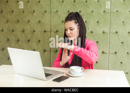 Time out! Ritratto di avvertenza attraente giovane donna freelancer nero con dreadlocks acconciatura in rosa camicetta, seduta in cafe e rendendo la chiamata video Foto Stock