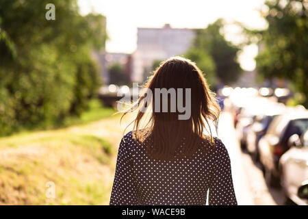 Vista posteriore della donna a piedi attraverso una strada di città sulla giornata di sole Foto Stock