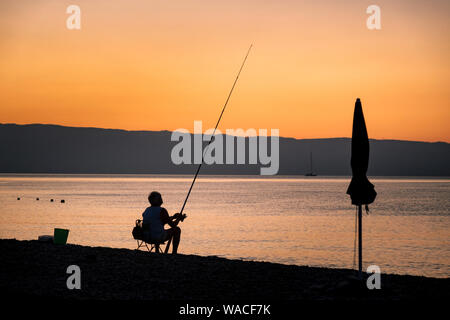 Silhouette di un pescatore in attesa sulla spiaggia al tramonto, Sicilia Foto Stock