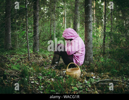 Persona confusa è andato alla raccolta dei funghi e sono andati persi nella foresta, disorientati spaventati e confusi, Nord Europa, sedersi sotto agli alberi. Persona persa in Foto Stock