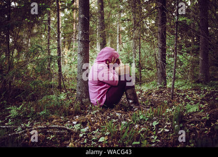 Persona confusa è andato alla raccolta dei funghi e sono andati persi nella foresta, disorientati spaventati e confusi, Nord Europa, sedersi sotto agli alberi. Persona persa in Foto Stock