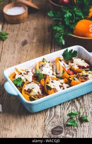 Arancione Farcite i peperoni con la carne macinata e mozzarella in piatto di ceramica su tavola in legno rustico Foto Stock