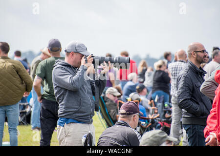 Un fotografo con una grande lente di scatto a un evento con la folla intorno (solo uso editoriale) Foto Stock