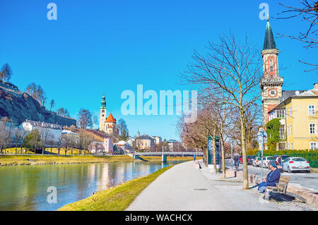 Salisburgo, Austria - 27 febbraio 2019: la vista panoramica sul fiume Salzach terrapieno con alti campanili delle chiese medievali ed accogliente prom pedonale Foto Stock