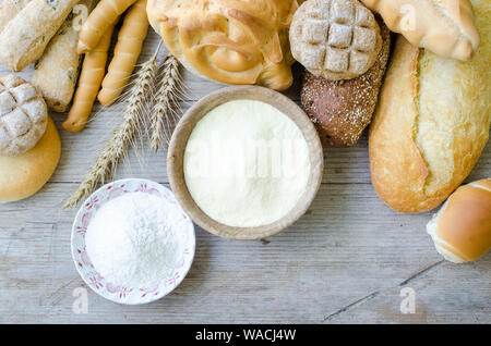 Diversi tipi di Italiano tradizionale di pane appena sfornato, vari tipi di pane e panini con ciotola di farina a fontana sul tavolo di legno dello sfondo. Rustico stile vintage. Vista dall'alto. Foto Stock