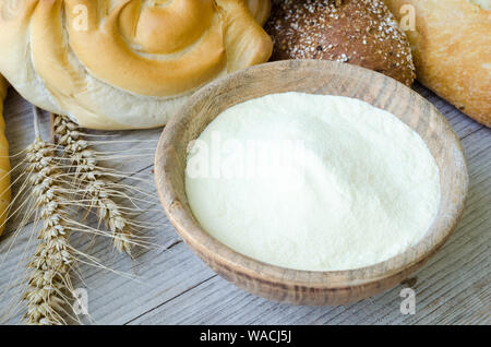 Diversi tipi di Italiano tradizionale di pane appena sfornato, vari tipi di pane e panini con ciotola di farina a fontana sul tavolo di legno dello sfondo. Rustico stile vintage. Foto Stock