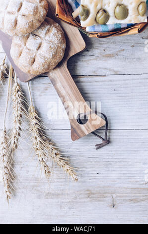 Assortimento di Italiano tradizionale di pane appena sfornato pane croccante di pane e panini con orecchie sul tavolo di legno dello sfondo. Focaccia alle olive. Vin rustico Foto Stock