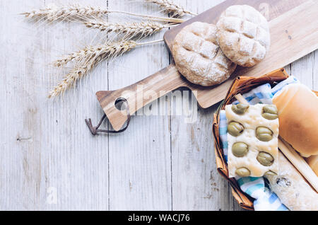 Assortimento di Italiano tradizionale di pane appena sfornato pane croccante di pane e panini con orecchie sul tavolo di legno dello sfondo. Focaccia alle olive. Vin rustico Foto Stock