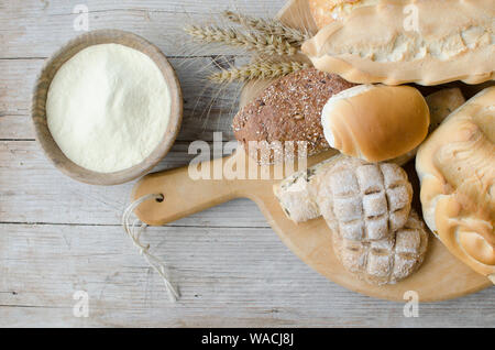 Diversi tipi di Italiano tradizionale di pane appena sfornato, vari tipi di pane e panini con ciotola di farina a fontana sul tavolo di legno dello sfondo. Rustico stile vintage. Vista dall'alto. Foto Stock