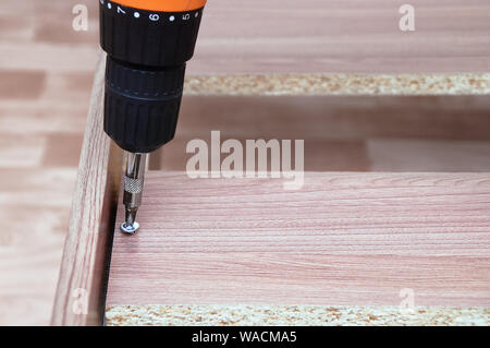 Montaggio di mobili. Trapano elettrico vicino. Le viti la vite in una tavola di legno. Foto Stock