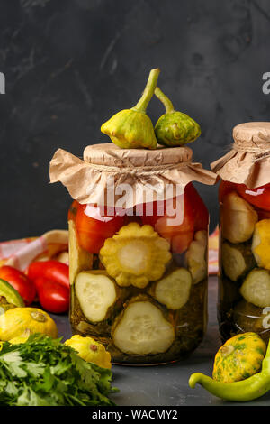 Un assortimento di cetrioli sottaceto, patissons e i pomodori in vasi su uno sfondo scuro, con orientamento verticale, close-up Foto Stock