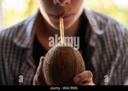 Giovane uomo in possesso di una noce di cocco con una cannuccia e bere, close up Foto Stock