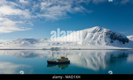 Barca su un mare tranquillo, in background ci sono montagna ricoperte di neve Foto Stock