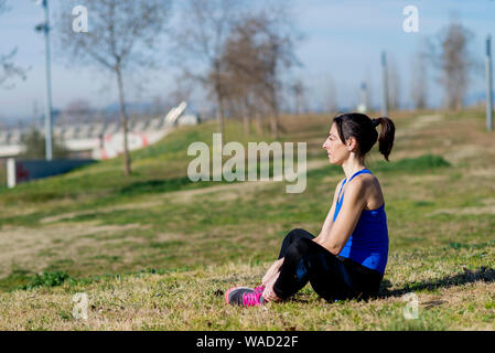 Atleta femminile meditando seduto su erba al parco nella giornata di sole Foto Stock