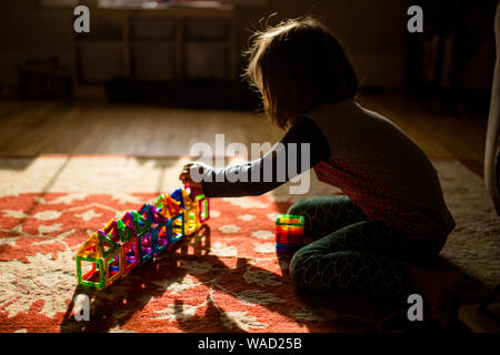 Un bambino si siede sul pavimento in golden morning light building con piastrelle Foto Stock