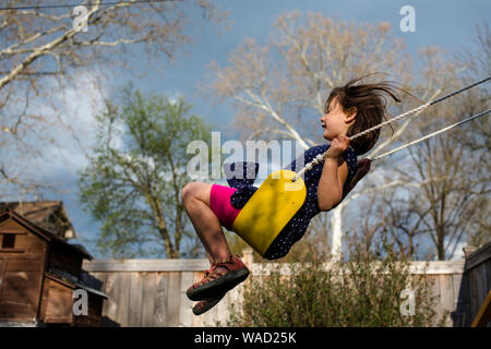 Una ragazza felice su uno swing giallo su un arioso stormy giornata di primavera Foto Stock