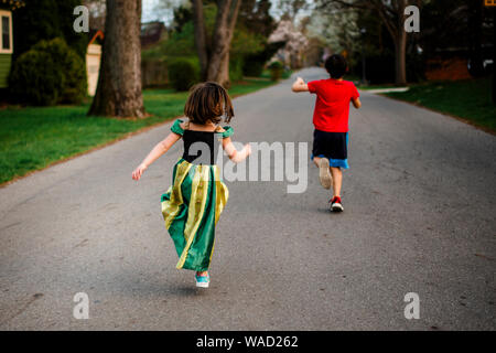 Due bambini saltare allegramente giù per una strada alberata in primavera Foto Stock