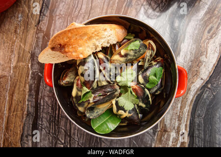 Cozze cotte con salsa al curry e servita nella pentola di metallo, stile asiatico cibo Foto Stock