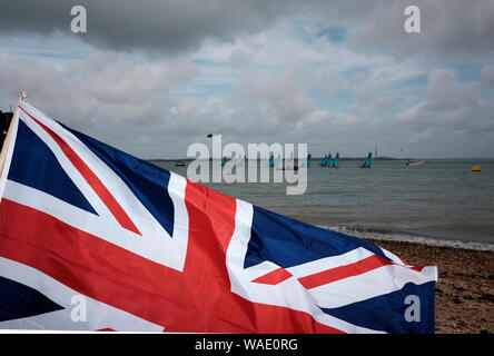 Small double hull yacht racing appena fuori dalla spiaggia sul lungomare di Cowes sull'Isola di Wight durante la Cowes Week Foto Stock