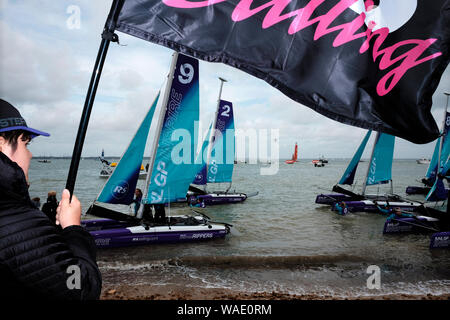 Small double hull yacht racing appena fuori dalla spiaggia sul lungomare di Cowes sull'Isola di Wight durante la Cowes Week Foto Stock