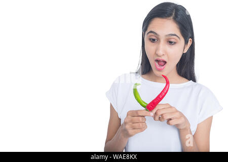 Bruna giovane ragazza con il rosso e il peperone verde peperoncino con espressioni di sorpresa sul suo viso isolati su sfondo bianco, food concept Foto Stock