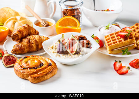 Tavolo per la colazione con i fiocchi d'avena, focaccine, croissant e frutta. Sfondo bianco. Foto Stock