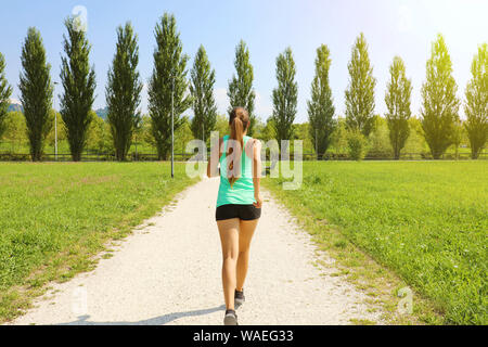 Giovane donna sportiva in esecuzione nel parco. Ragazza Fitness jogging nel parco. Vista posteriore della ragazza sportiva in esecuzione sul percorso. Foto Stock