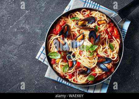 Gli spaghetti con le cozze in una piccante salsa di pomodoro in una padella su una tavola di cemento, vista orizzontale dal di sopra, flatlay, spazio vuoto Foto Stock