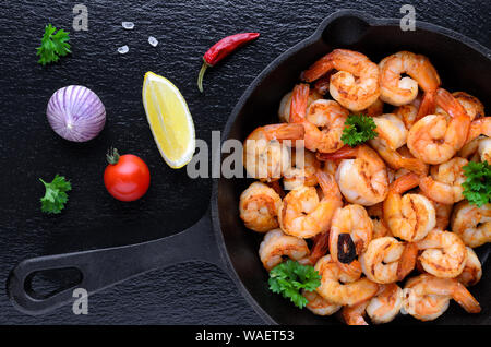 Gustoso arrosto di gamberi in una ghisa padella con prezzemolo e aglio, peperoncino, pomodoro con limone su sfondo nero Foto Stock