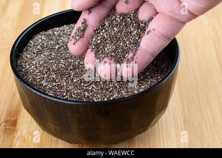 Semi di Chia sono versata da una palma umana in una ciotola. Close up. Foto Stock