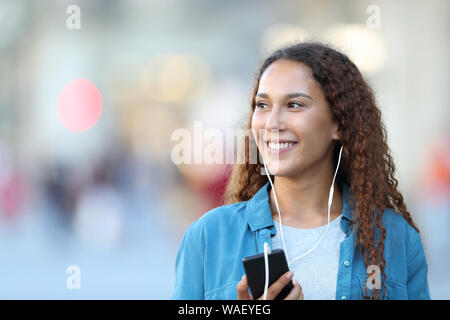 Vista frontale il ritratto di una razza mista donna ascoltando musica guardando al lato della strada Foto Stock