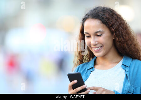 Felice razza mista donna utilizzando smart phone a piedi in strada Foto Stock