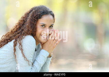 Ritratto di un felice razza mista donna posa guardando la telecamera seduto in un parco Foto Stock