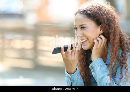 Felice di mixed-gara Donna che utilizza il riconoscimento vocale sul telefono intelligente per registrare i messaggi in un parco Foto Stock