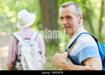 Ritratto di uomo anziano con zaino dietro la schiena guardando la fotocamera mentre si cammina nel bosco insieme con la donna Foto Stock