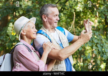 Senior sorridente uomo in piedi con il cellulare e scattare una foto della bellissima natura con i senior donna in piedi vicino a lui e sorridente Foto Stock