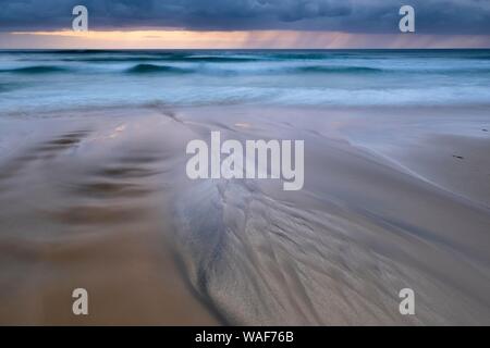 L'acqua scorre su strutture bizzarre sulla spiaggia sabbiosa, pioggia nuvole sopra il mare, Dalmore Beach, isola di Lewis, Scozia Foto Stock