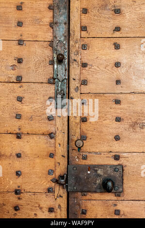 Una vecchia porta di legno con le viti in ferro e in vecchio stile serratura con anche un piccolo blocco moderno. Foto Stock