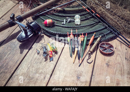 Canna da pesca, mulinello, galleggianti e affrontare background sul pontile in legno dal fiume Foto Stock