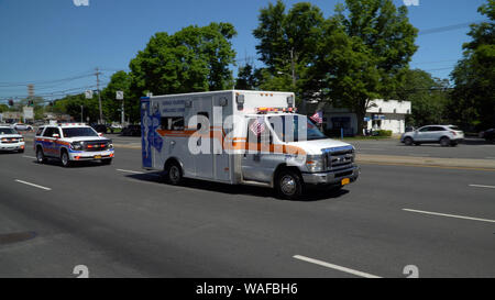 Long Island, NY - Circa 2019: il volontariato locale ambulanza carrello aziona verso il basso strada chiusa per la piccola città di memorial day parade celebrazione in onore di American Foto Stock