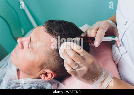 Trattamento della calvizie con iniezioni di bellezza. Cosmetologo mani guanti nel fare una iniezione sottocutanea. Plasmalifting paziente di sesso maschile Foto Stock