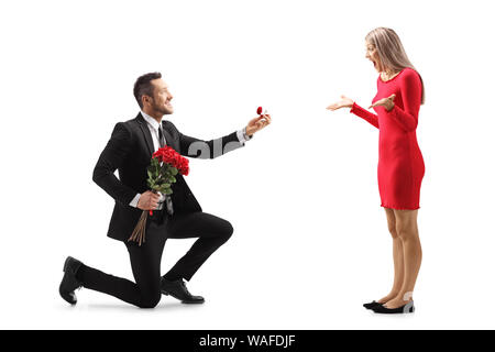 Giovane uomo inginocchiato con le rose e un anello di fidanzamento e proponendo una sorpresa giovane donna isolato su sfondo bianco Foto Stock